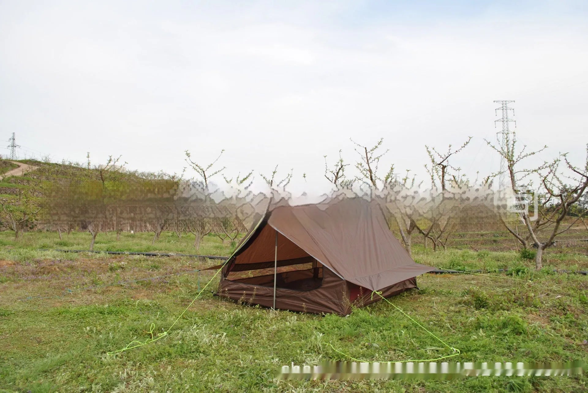 Brown A-line tent pitched with hiking poles, showing guy lines and aluminium ground nails.