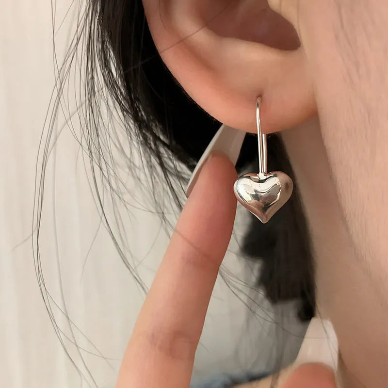 Pair of silver-tone 3D glossy heart-shaped drop earrings on a white background.