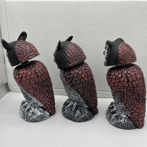 A detailed artificial owl bird scare ornament with a shaking head, shown in a garden setting.
