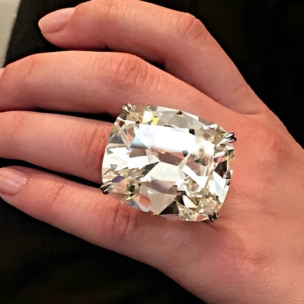 Simple white gold colour alloy ring with an inlaid square diamond, shown on a finger.