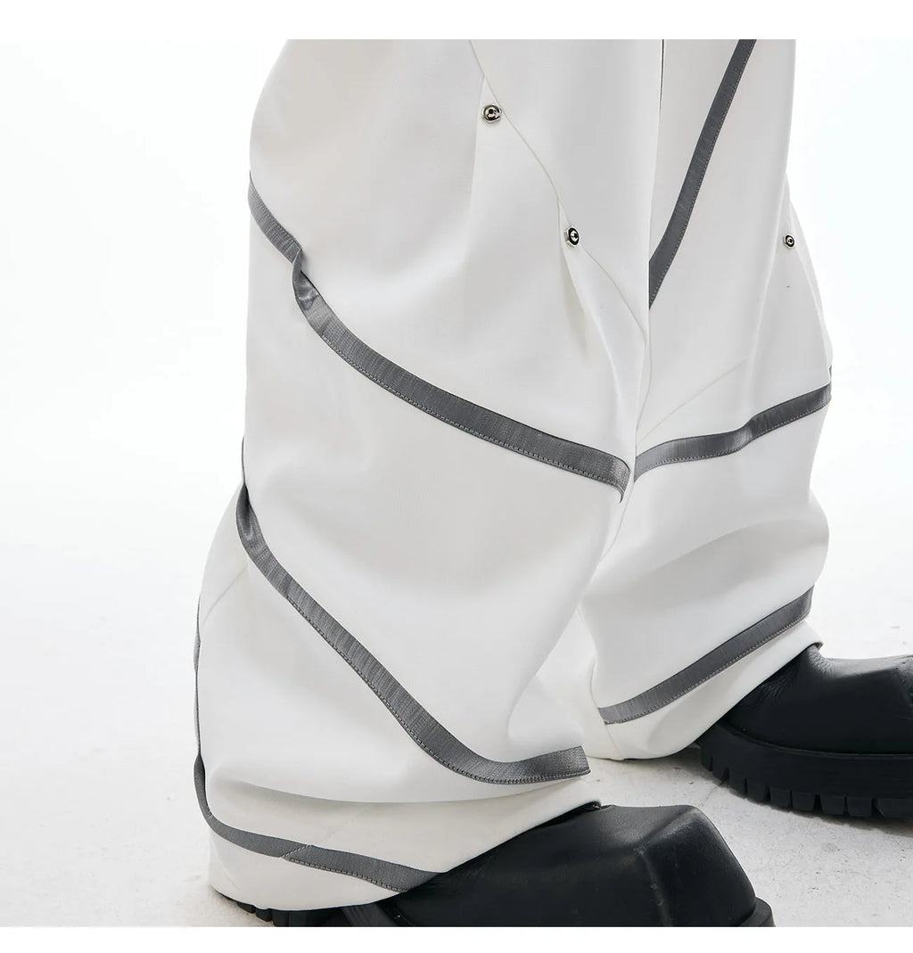 Men's black trousers with a deconstructing three-dimensional cut and pleats secured with metal striped rivets.
