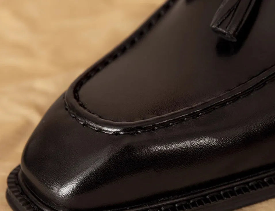 Men's black leather slip-on loafers with a fringed detail on the vamp and a rubber sole.