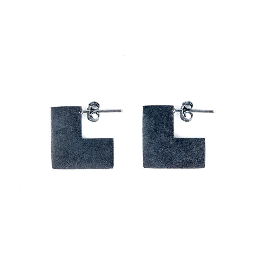 Close-up of oxidised black geometric square sterling silver ring-style earrings on a grey background.