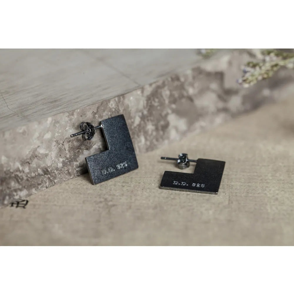 Close-up of oxidised black geometric square sterling silver ring-style earrings on a grey background.