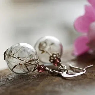 Close-up of transparent glass dandelion seed earrings on a French hook in silver finish.