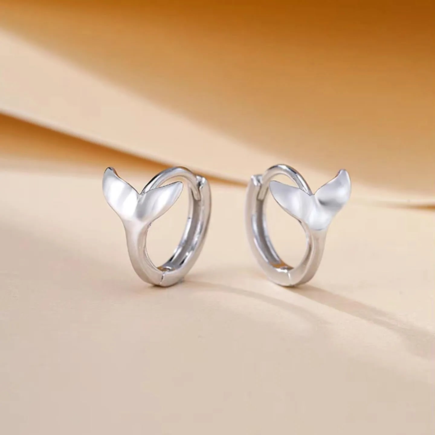 A pair of simple women's fishtail earrings in electroplated copper, shown in white gold colour.
