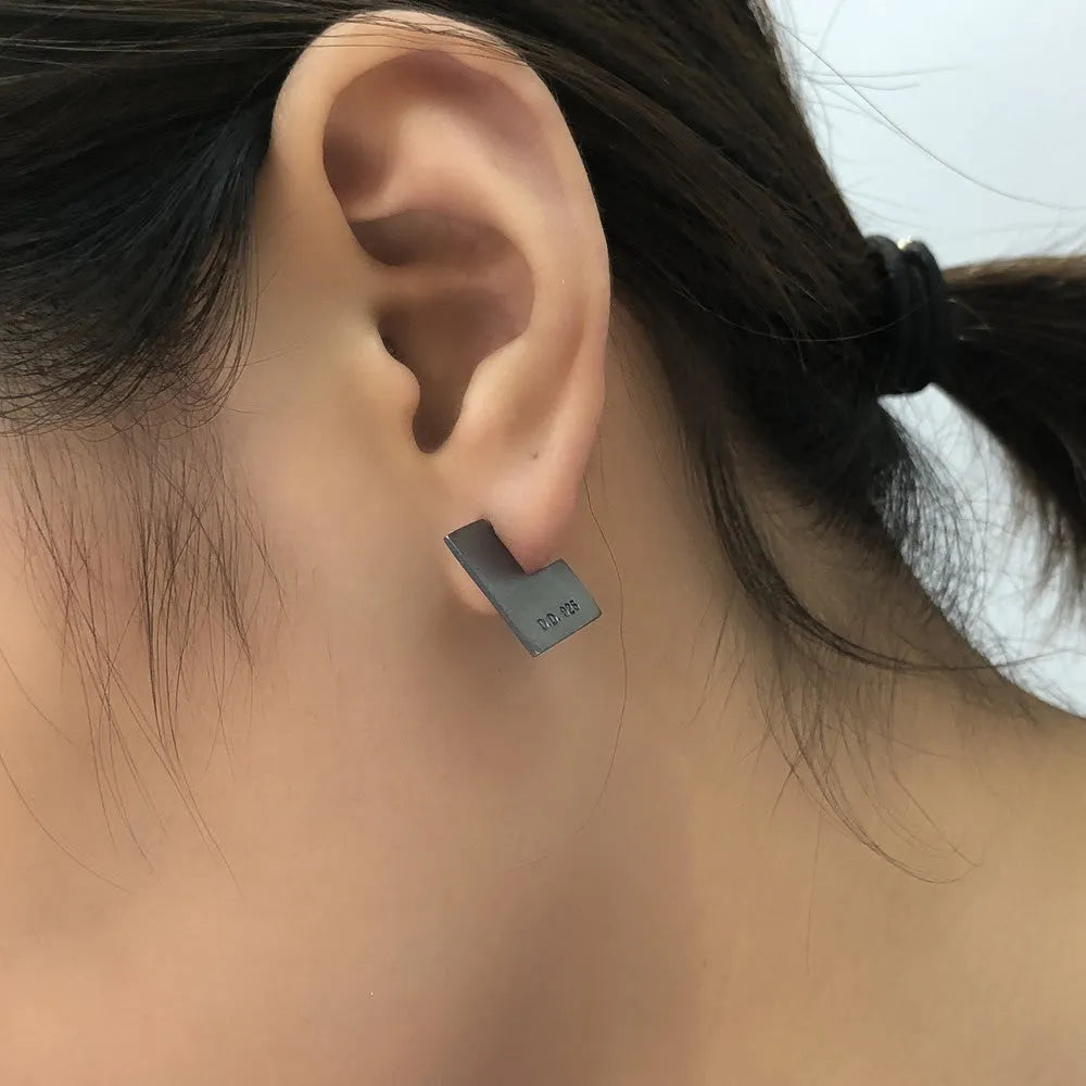 Close-up of oxidised black geometric square sterling silver ring-style earrings on a grey background.