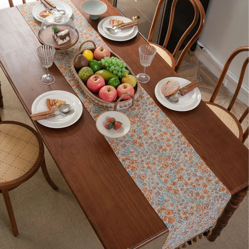 Beige jacquard table runner with long tassels and floral leaf pattern laid on a dining table.
