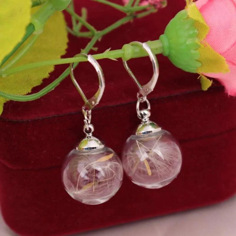 Close-up of transparent glass dandelion seed earrings on a French hook in silver finish.