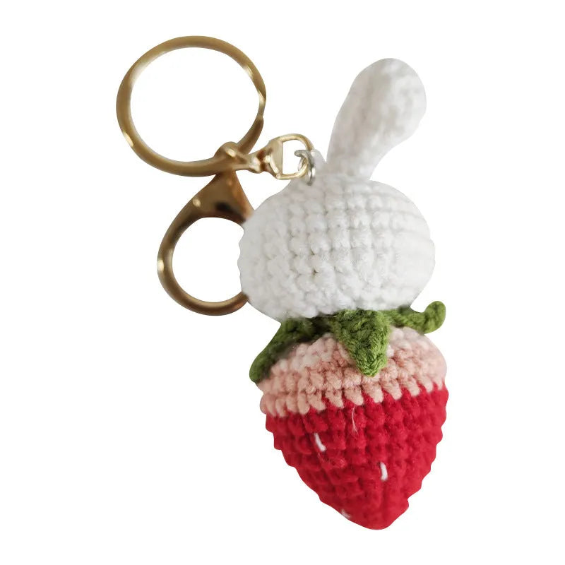 White hand-woven rabbit and strawberry wire pendant on a key against a plain background.