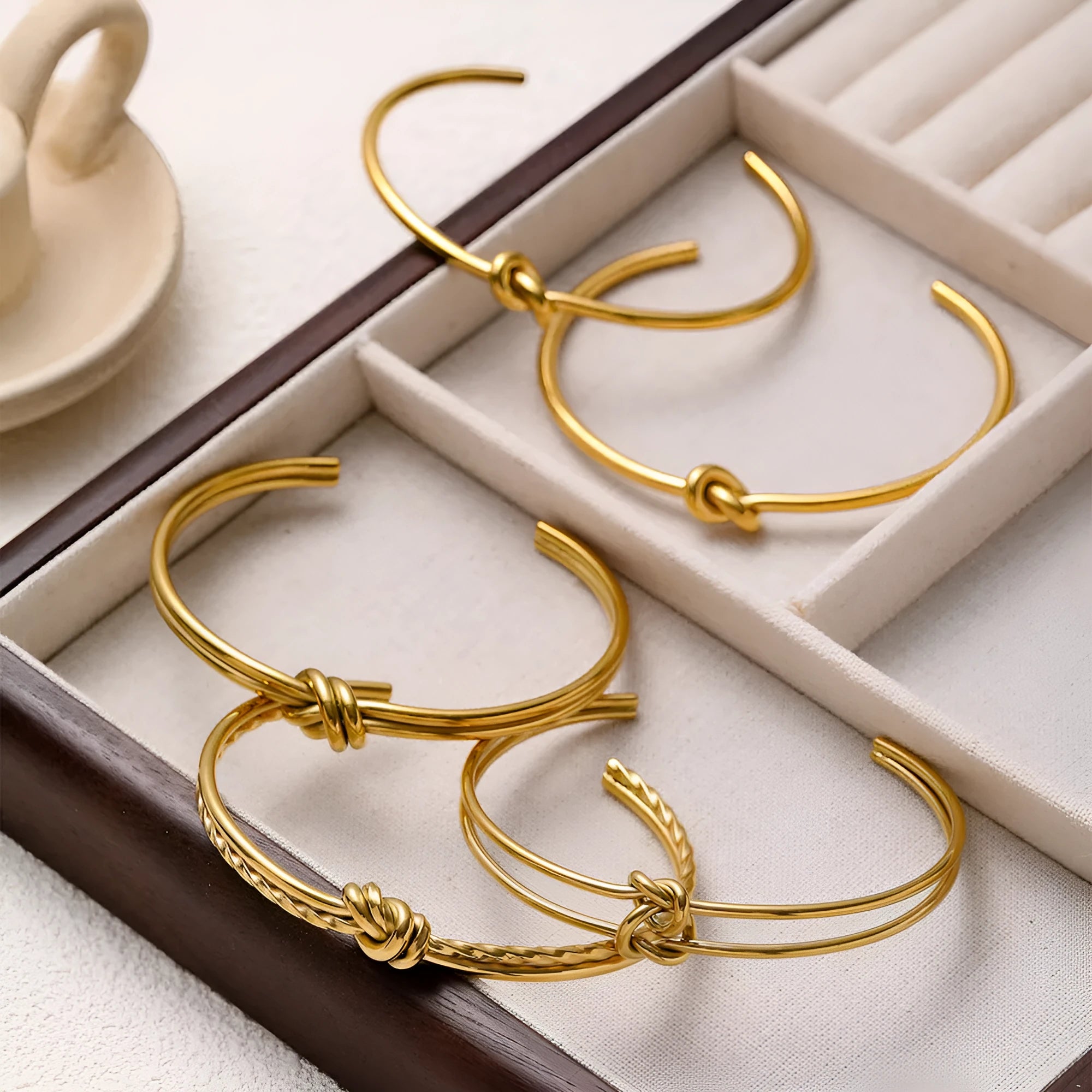 Adjustable stainless steel women's bracelet with gold plating and a double-layer knotted C-shape design.