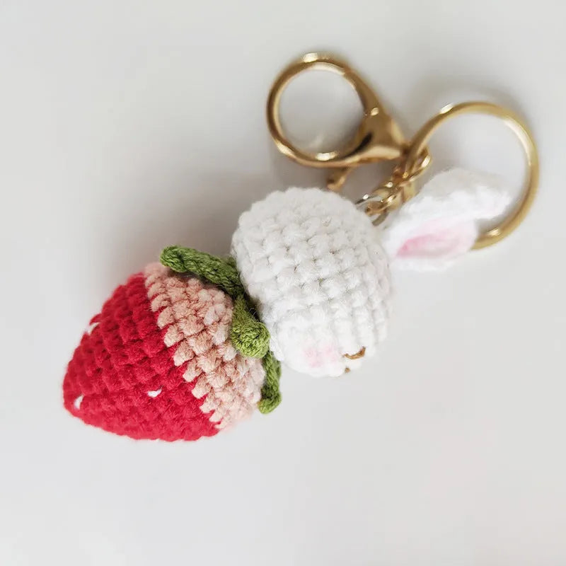 White hand-woven rabbit and strawberry wire pendant on a key against a plain background.