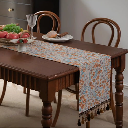 Beige jacquard table runner with long tassels and floral leaf pattern laid on a dining table.