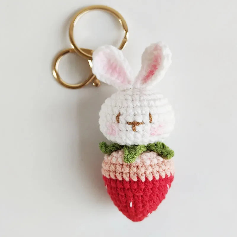 White hand-woven rabbit and strawberry wire pendant on a key against a plain background.