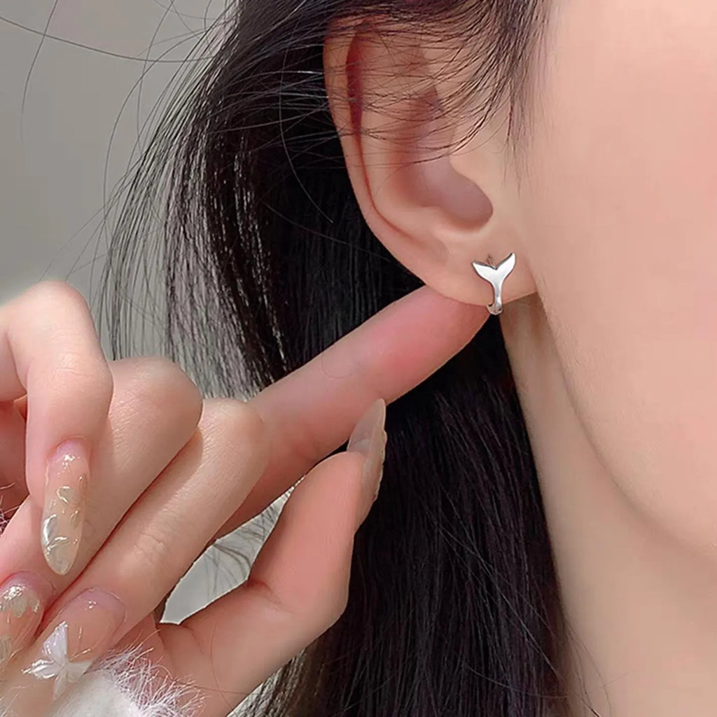 A pair of simple women's fishtail earrings in electroplated copper, shown in white gold colour.