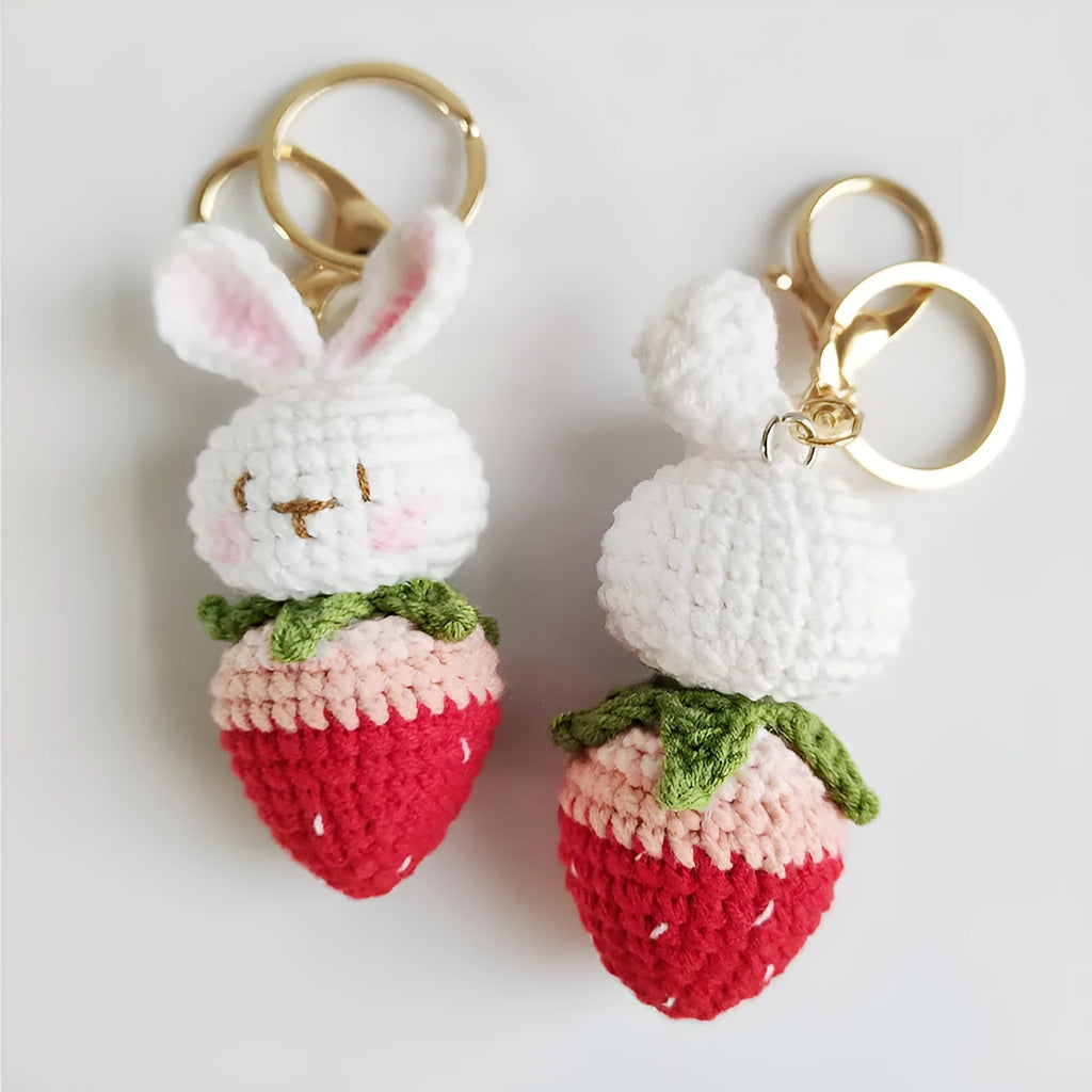 White hand-woven rabbit and strawberry wire pendant on a key against a plain background.