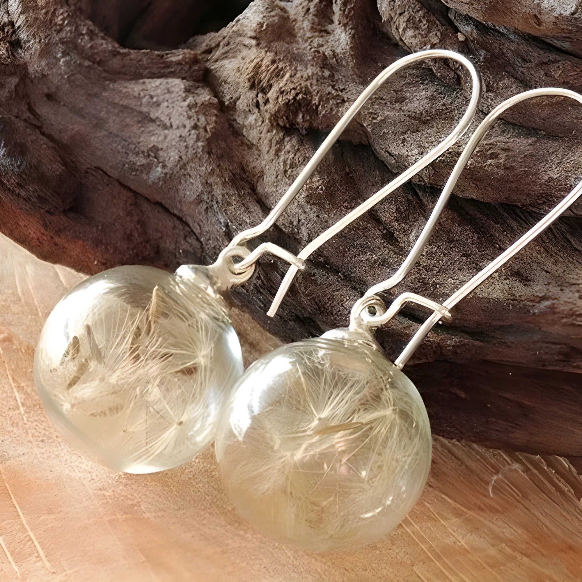 Close-up of transparent glass dandelion seed earrings on a French hook in silver finish.