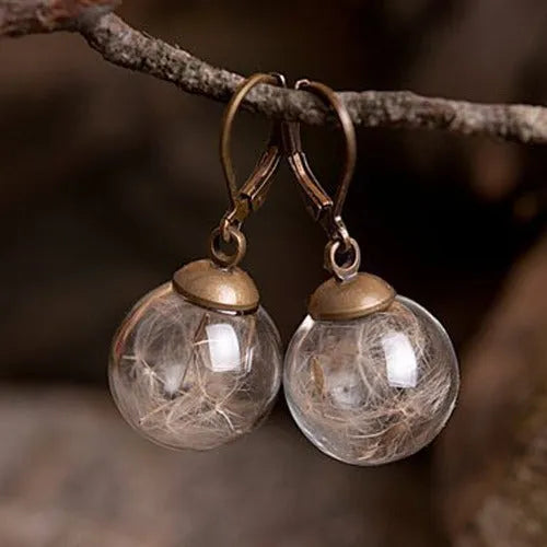 Close-up of transparent glass dandelion seed earrings on a French hook in silver finish.