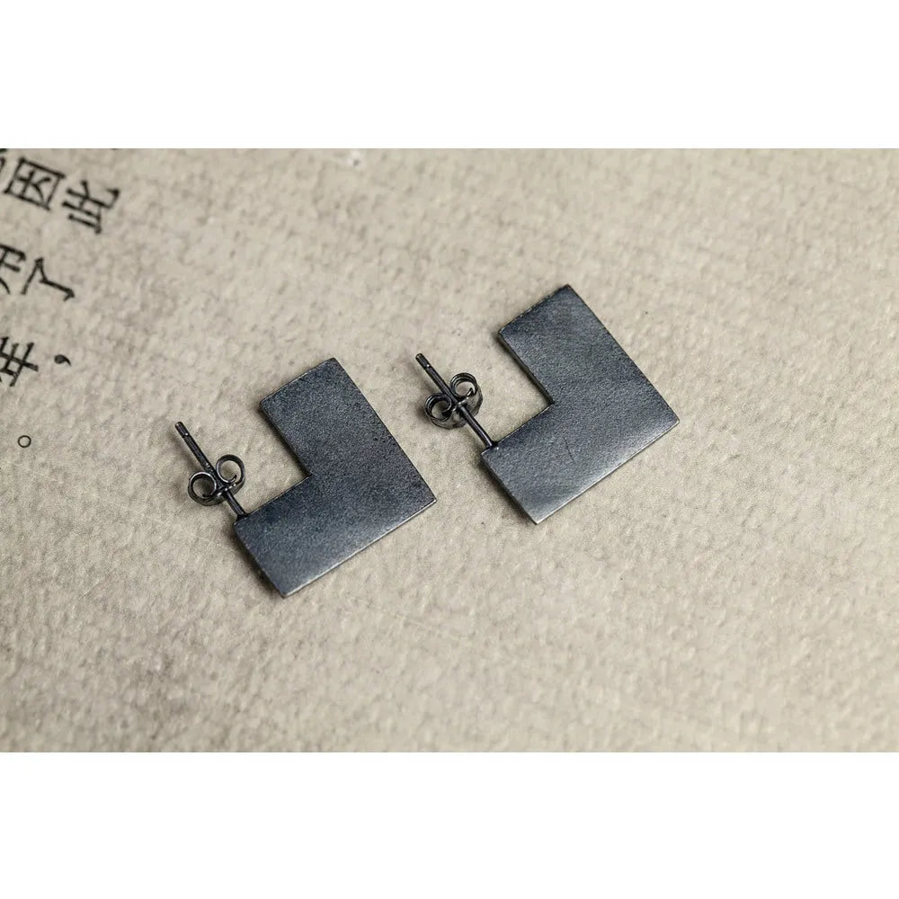 Close-up of oxidised black geometric square sterling silver ring-style earrings on a grey background.