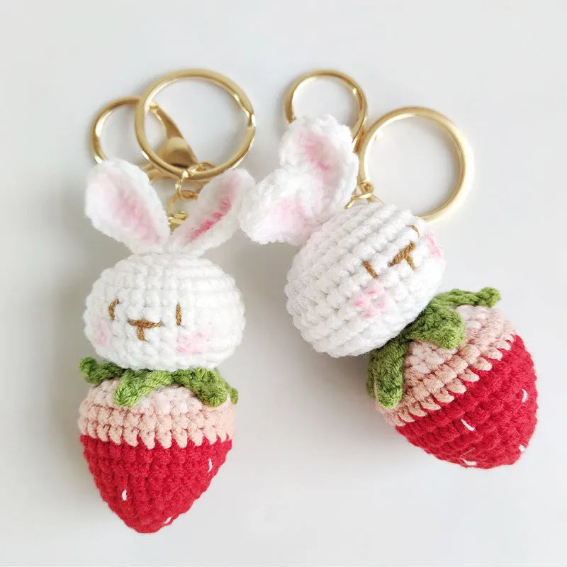 White hand-woven rabbit and strawberry wire pendant on a key against a plain background.