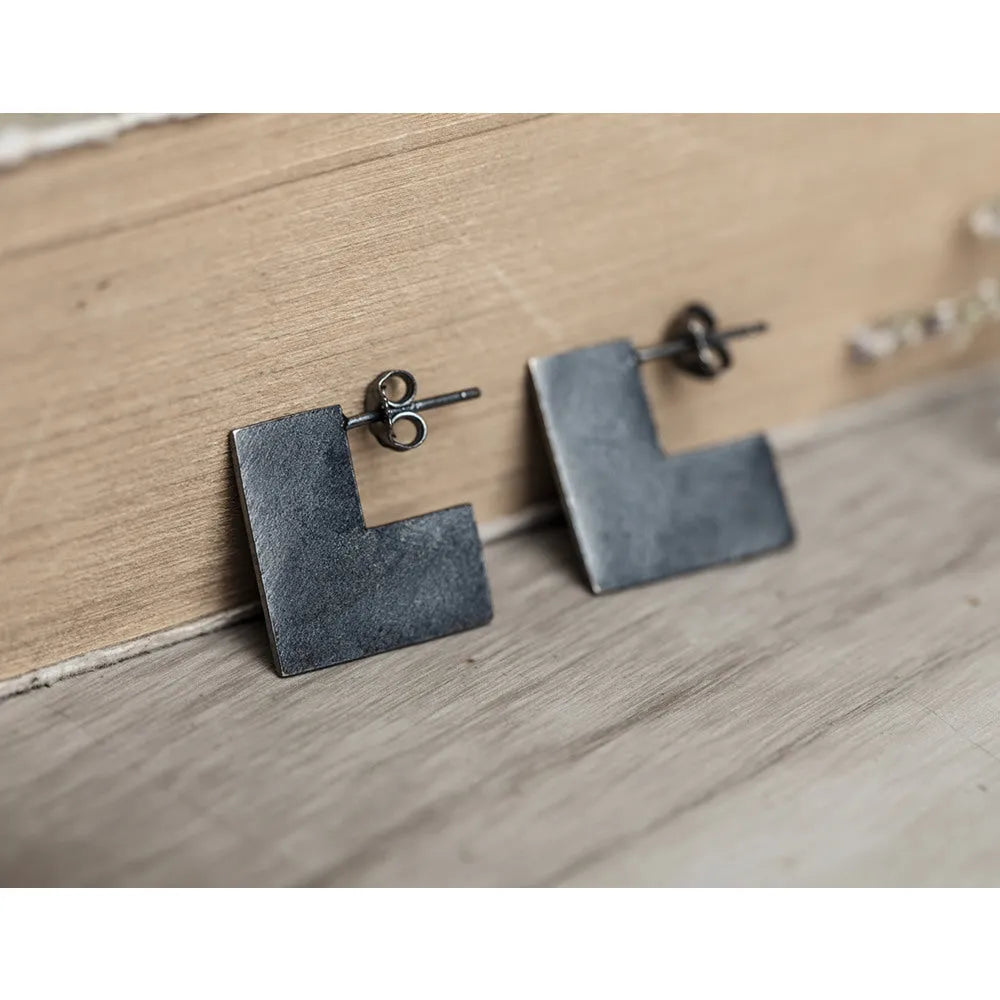 Close-up of oxidised black geometric square sterling silver ring-style earrings on a grey background.