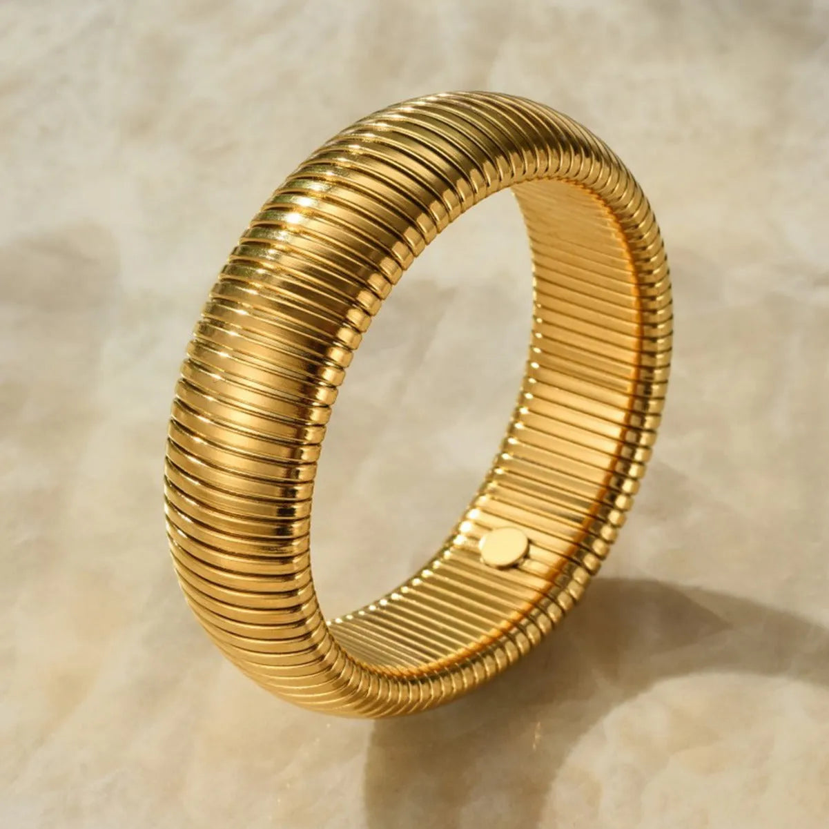Women's titanium steel bracelet with vertical stripe ring design in gold plating, shown on a wrist.