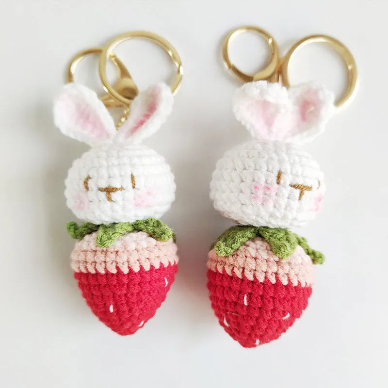 White hand-woven rabbit and strawberry wire pendant on a key against a plain background.