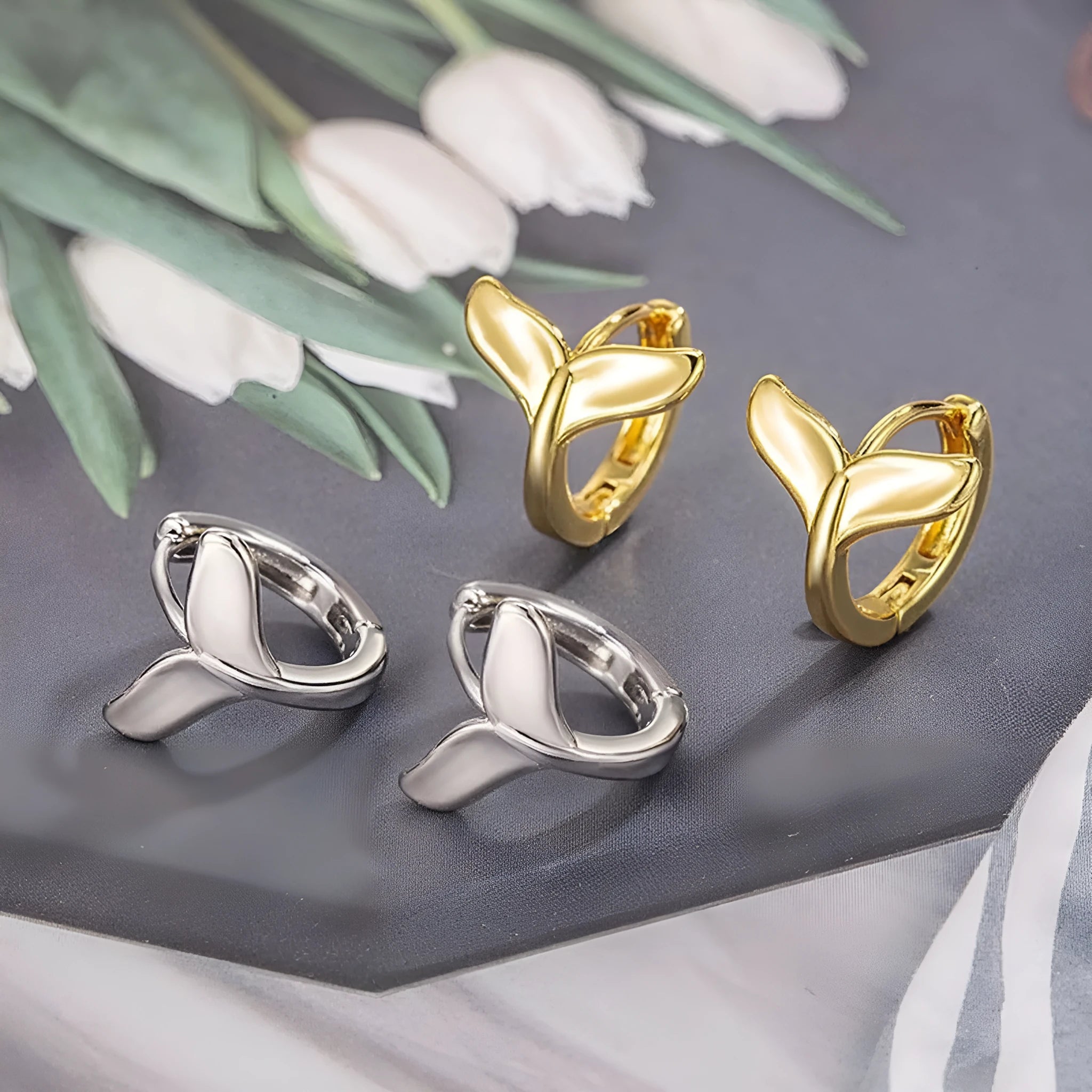 A pair of simple women's fishtail earrings in electroplated copper, shown in white gold colour.