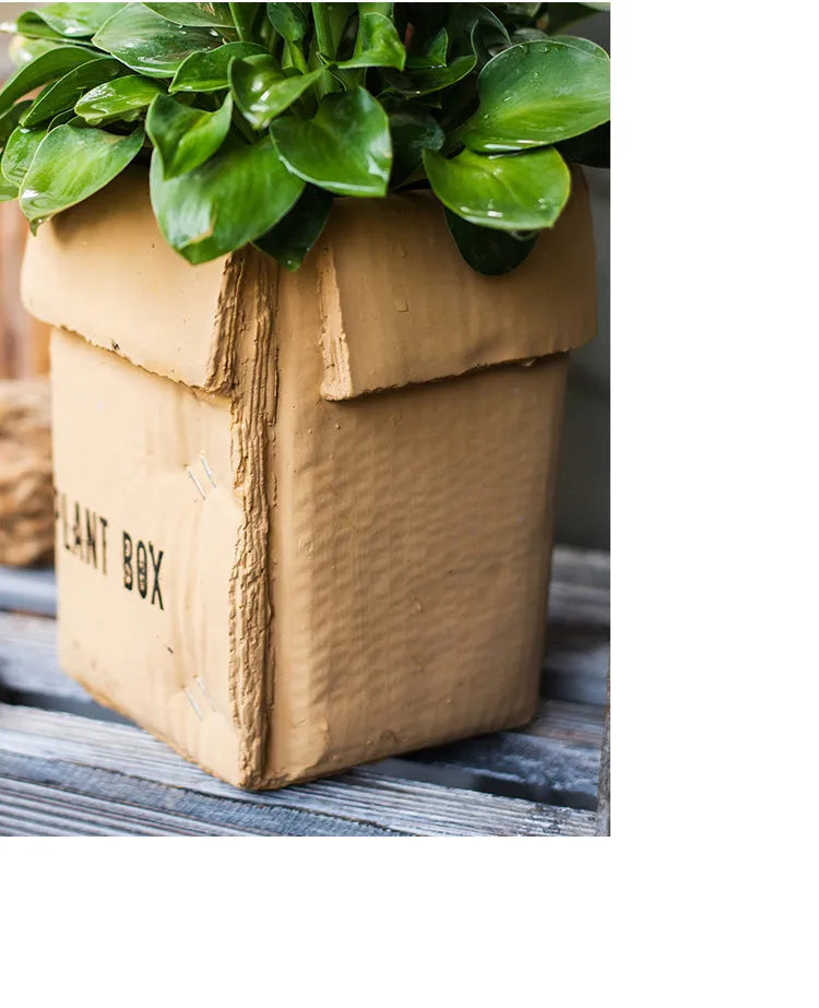 Cement brown paper box style flowerpot with angular sides and a perforated base on a floor.