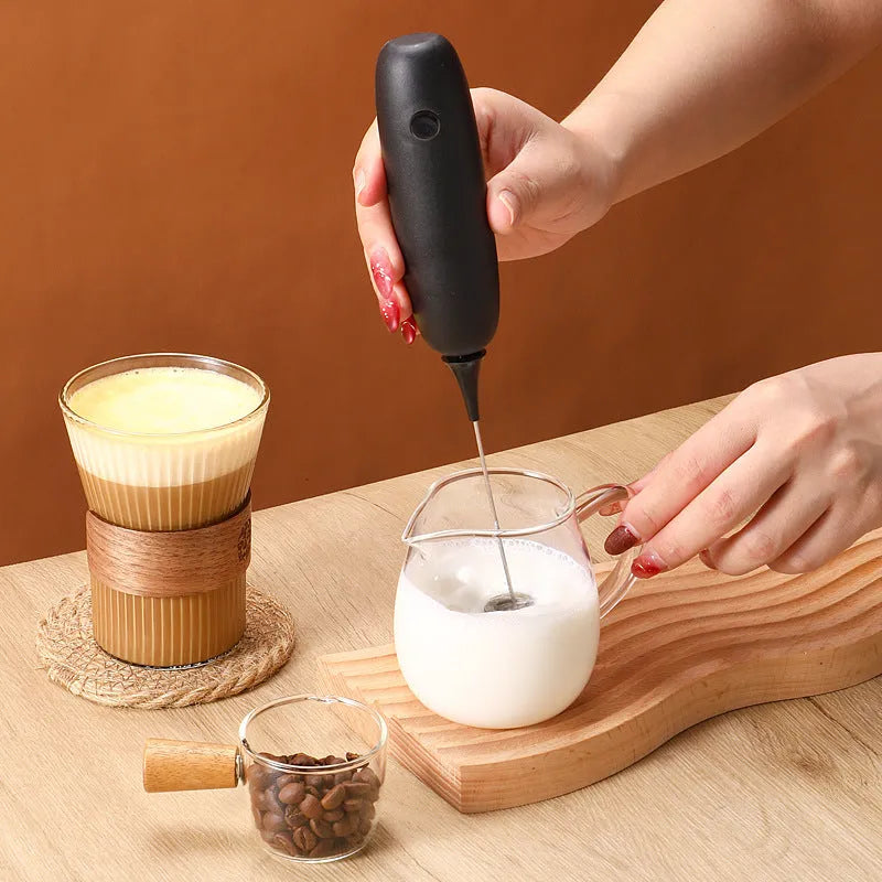 Black and white handheld electric milk frother and blender on a kitchen counter.