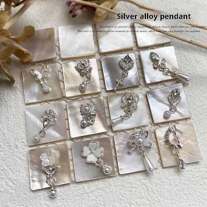Mixed silver alloy metal nail art pendants with tassel and pearl accents on white background