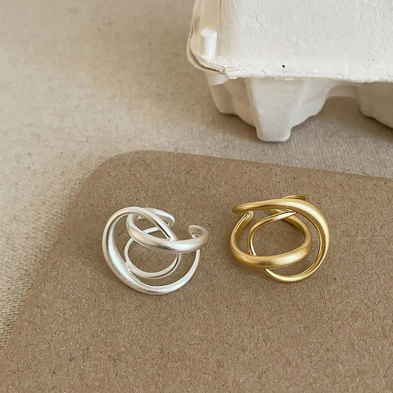 Geometric open ring for women with a 3D interlaced design in matte metal, shown in gold and silver finishes.