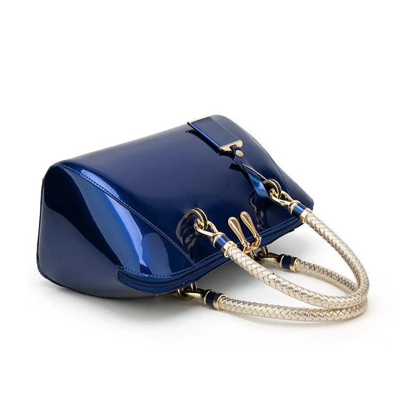 Shiny blue PVC patent leather handbag with lock closure and crossbody strap on a white background