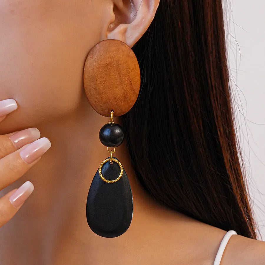 A pair of brown and black wooden ellipse earrings with a retro design on a plain background.