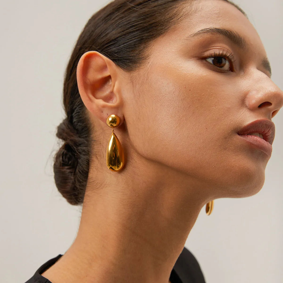 A pair of gold-coloured geometric earrings with a hemisphere base and dangling water drop pendant.