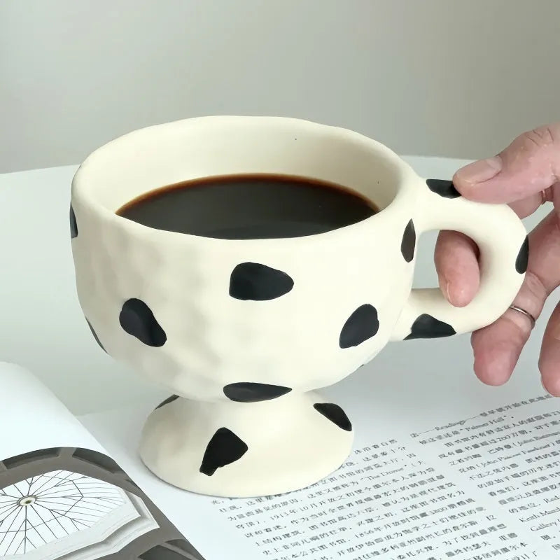 Handmade irregularly shaped ceramic mug in a solid colour, shown on a table.