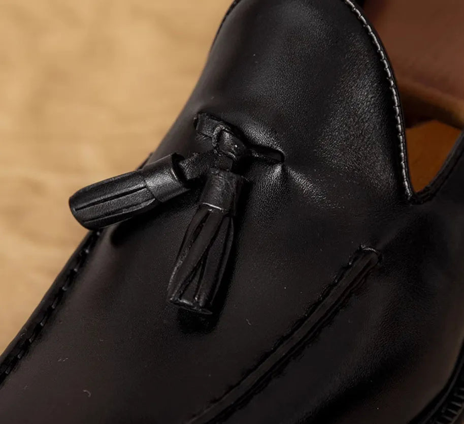 Men's black leather slip-on loafers with a fringed detail on the vamp and a rubber sole.