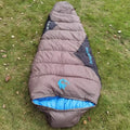 Brown cotton camping sleeping bag rolled next to its grey compression storage bag.