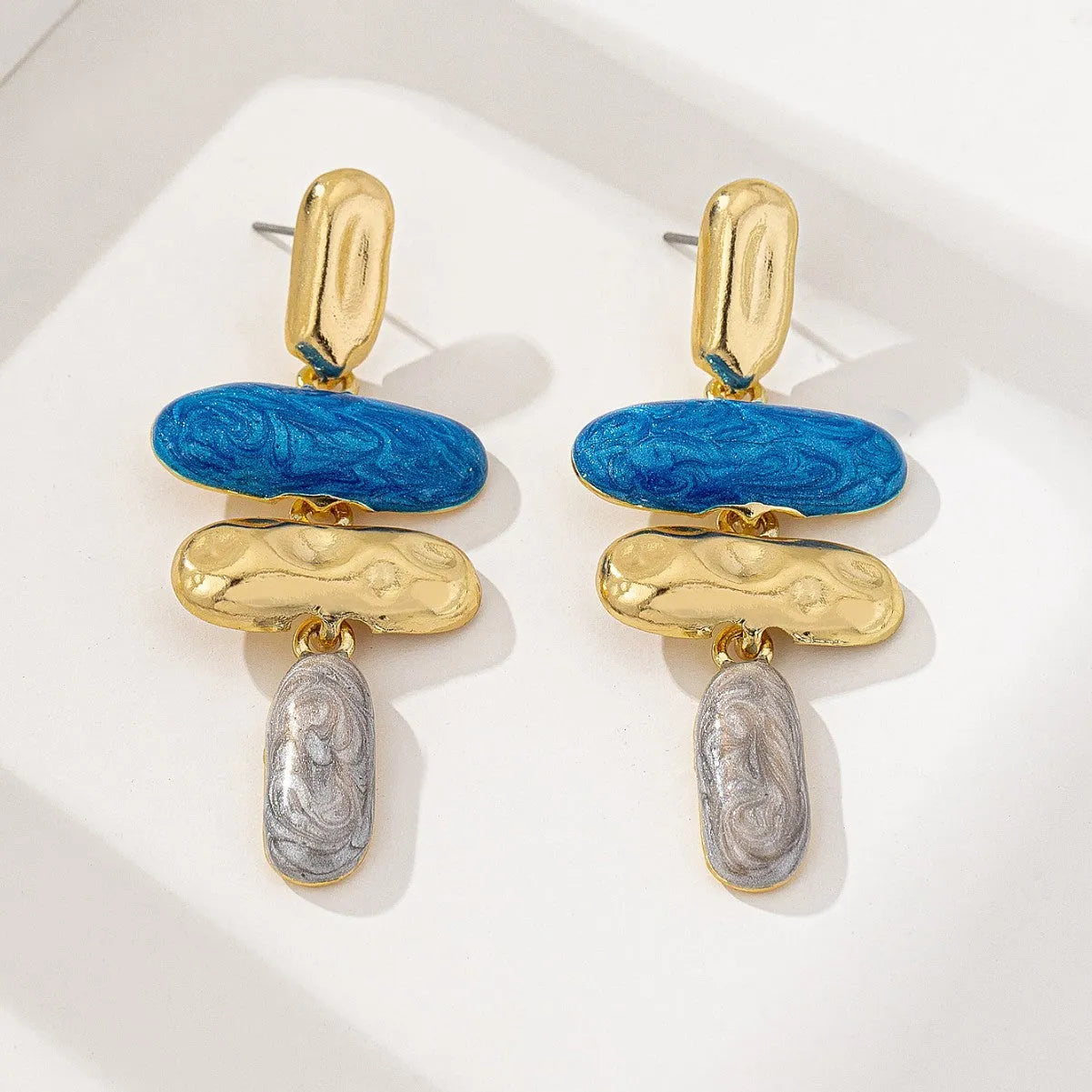 A pair of geometric-shaped stud earrings with a multicolour metallic finish on a plain background.