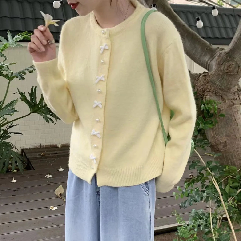 Women's light pink cardigan sweater with a black bow detail and pearl buttons on a hanger.