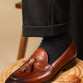 Men's black genuine leather tassel loafers on a solid background, showing polished upper and rubber sole.