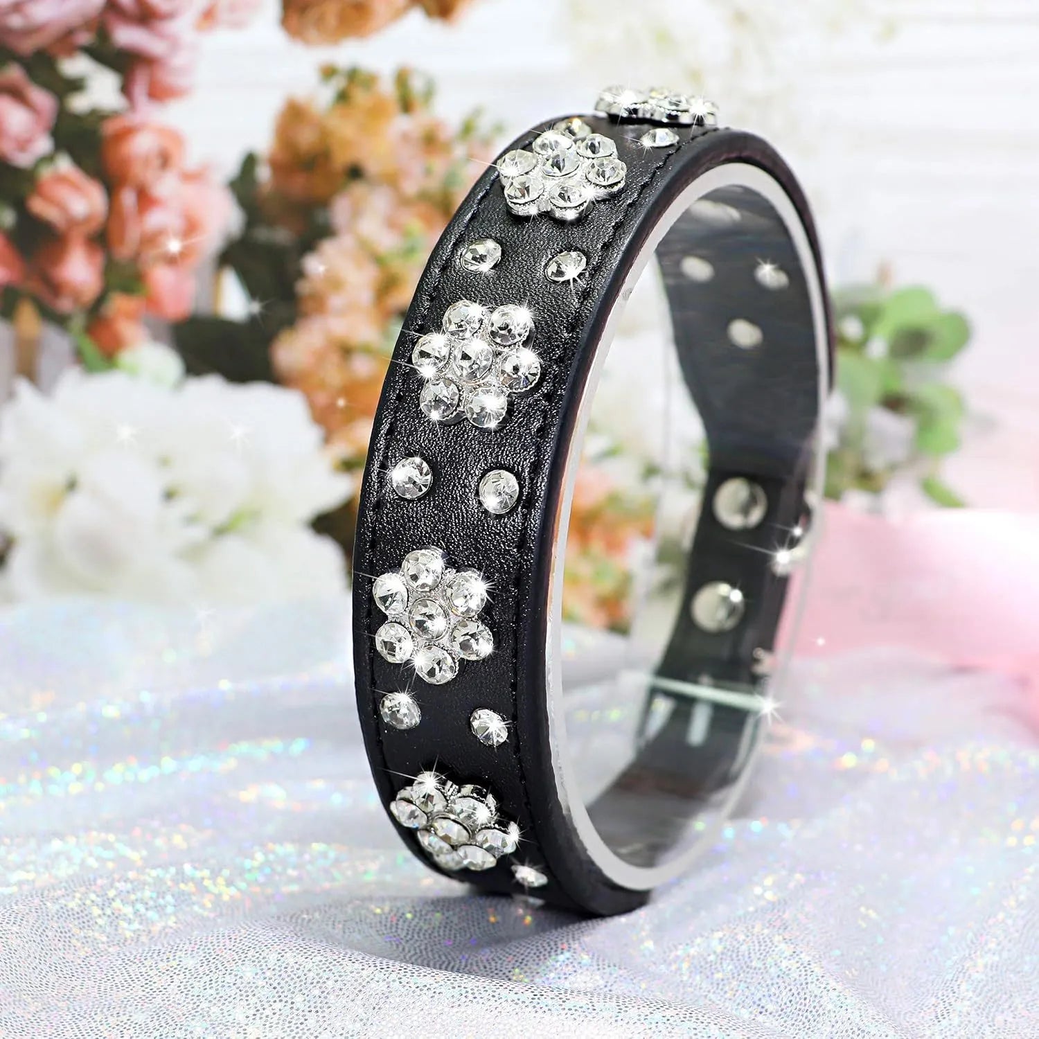 Close-up of a black PU leather dog collar with a rhinestone flower pattern and metal studs.