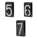 White solar powered illuminated house number sign with LED lights, mounted on a dark wall