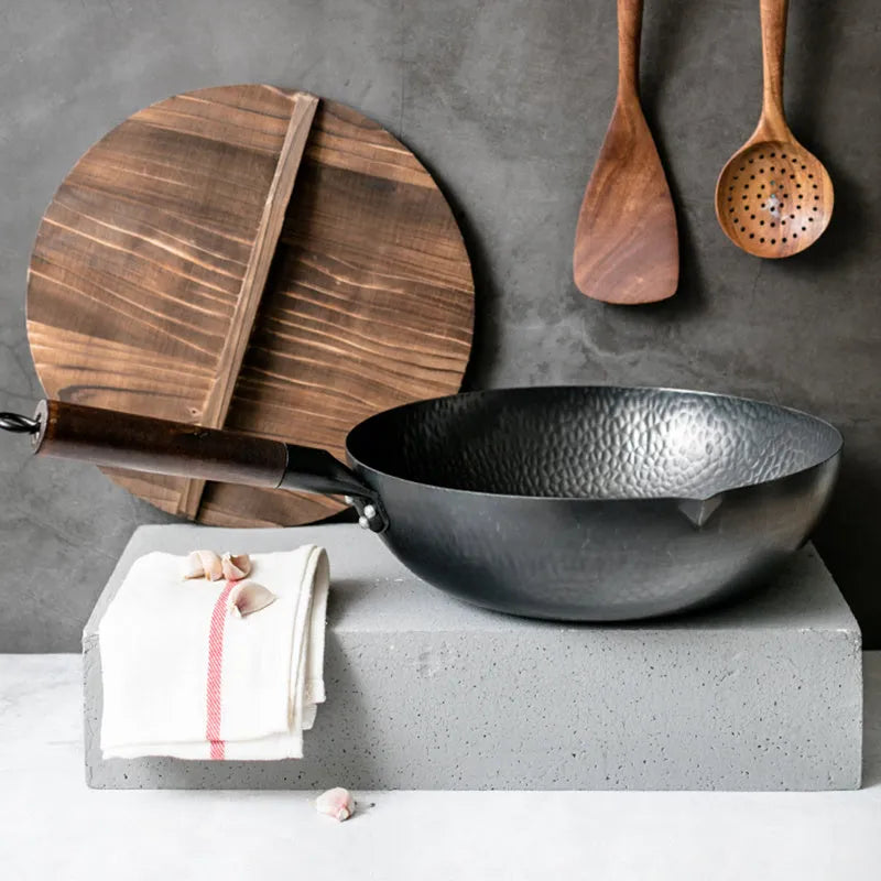 Black handmade traditional iron wok with a wooden handle on a stovetop.