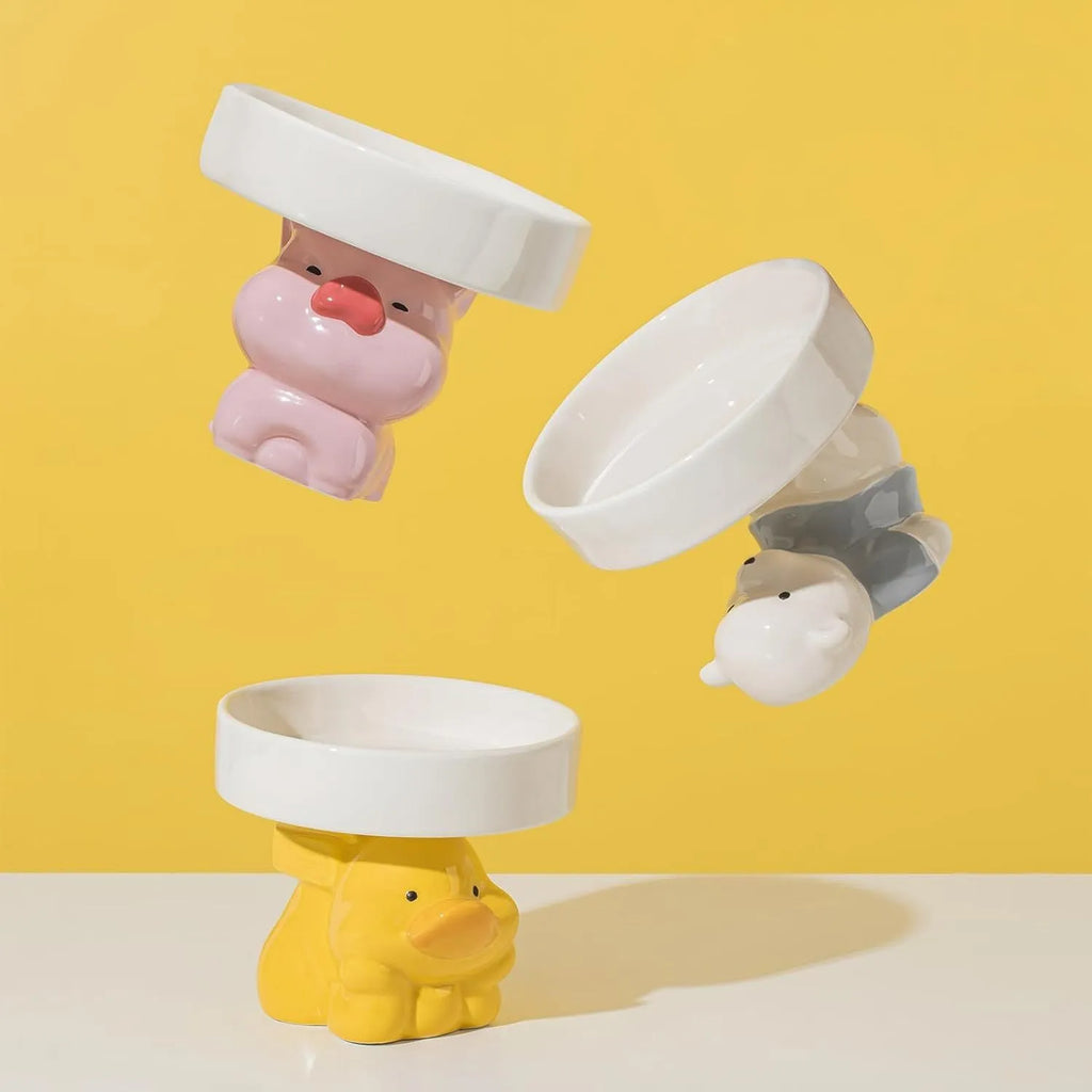 Raised ceramic cat bowl with animal design in pink, yellow, or white, showing wide rim.