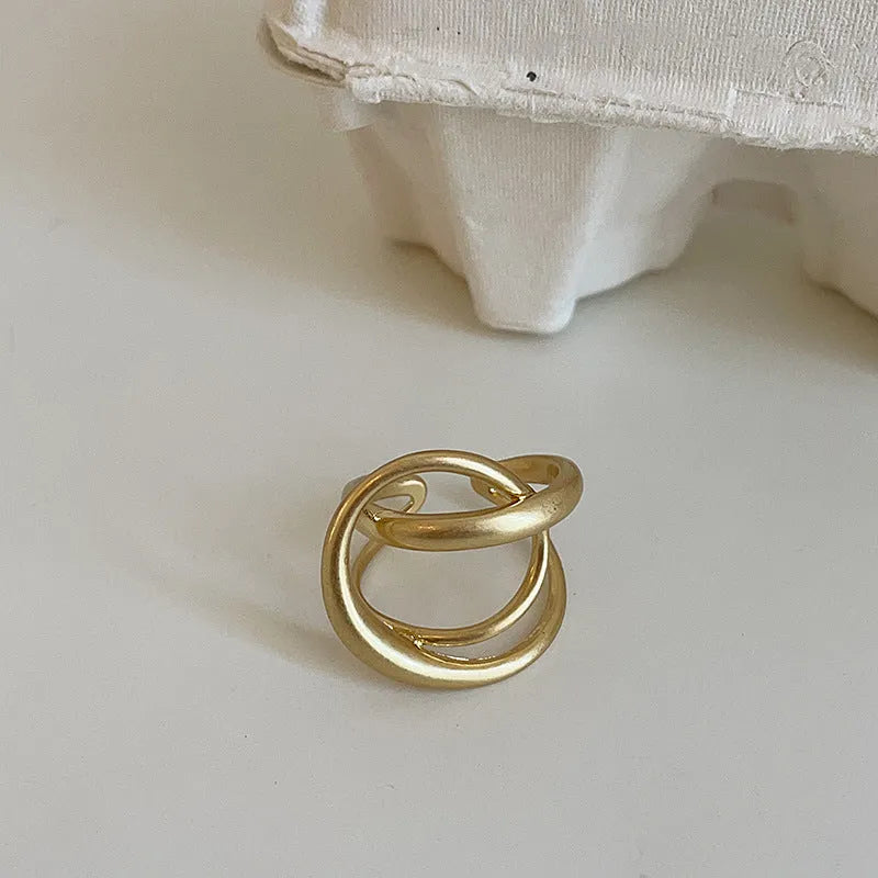 Geometric open ring for women with a 3D interlaced design in matte metal, shown in gold and silver finishes.