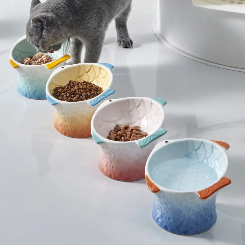 Blue fish-shaped ceramic cat bowl with tilted design and non-slip base on a wooden surface.