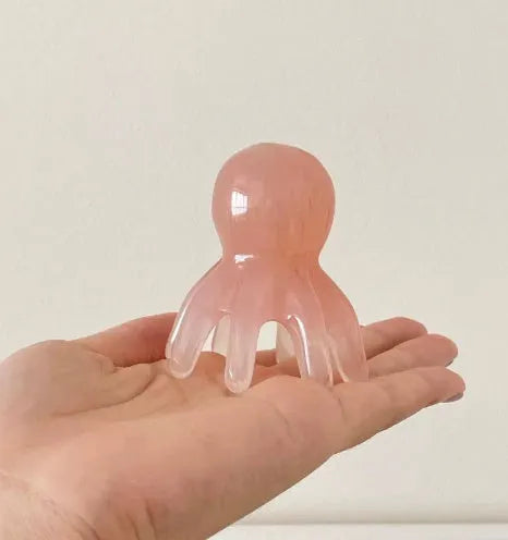 Small pink octopus-shaped massage comb made of natural resin with a storage bag.