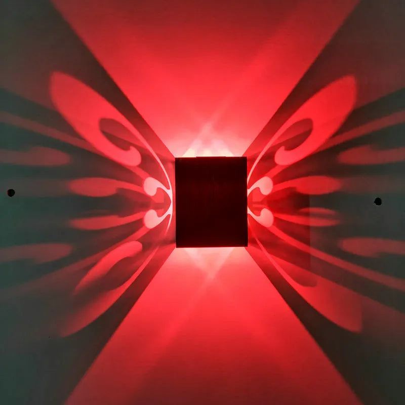 Modern aluminium butterfly-shaped LED wall lamp on a white wall with remote control.