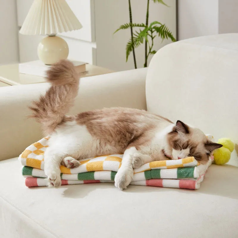 Green plaid pattern soft fleece pet blanket with fur ball decoration on a sofa